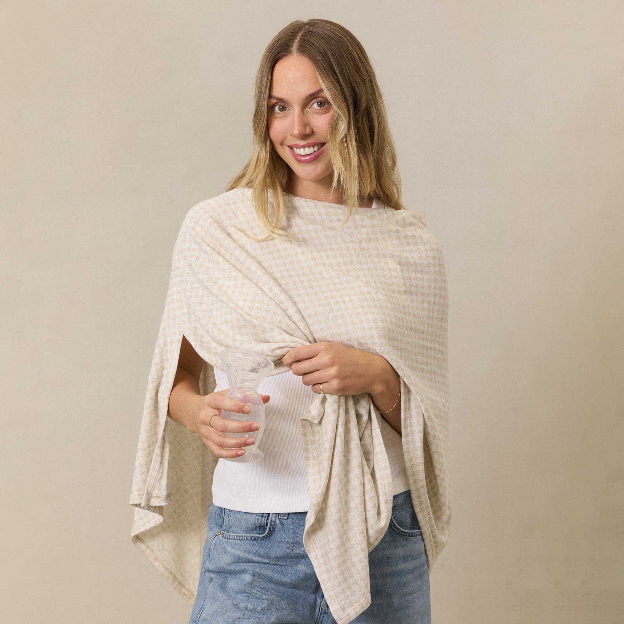 Woman using manual pump while wearing Solly Baby nursing cover in Cream Houndstooth.