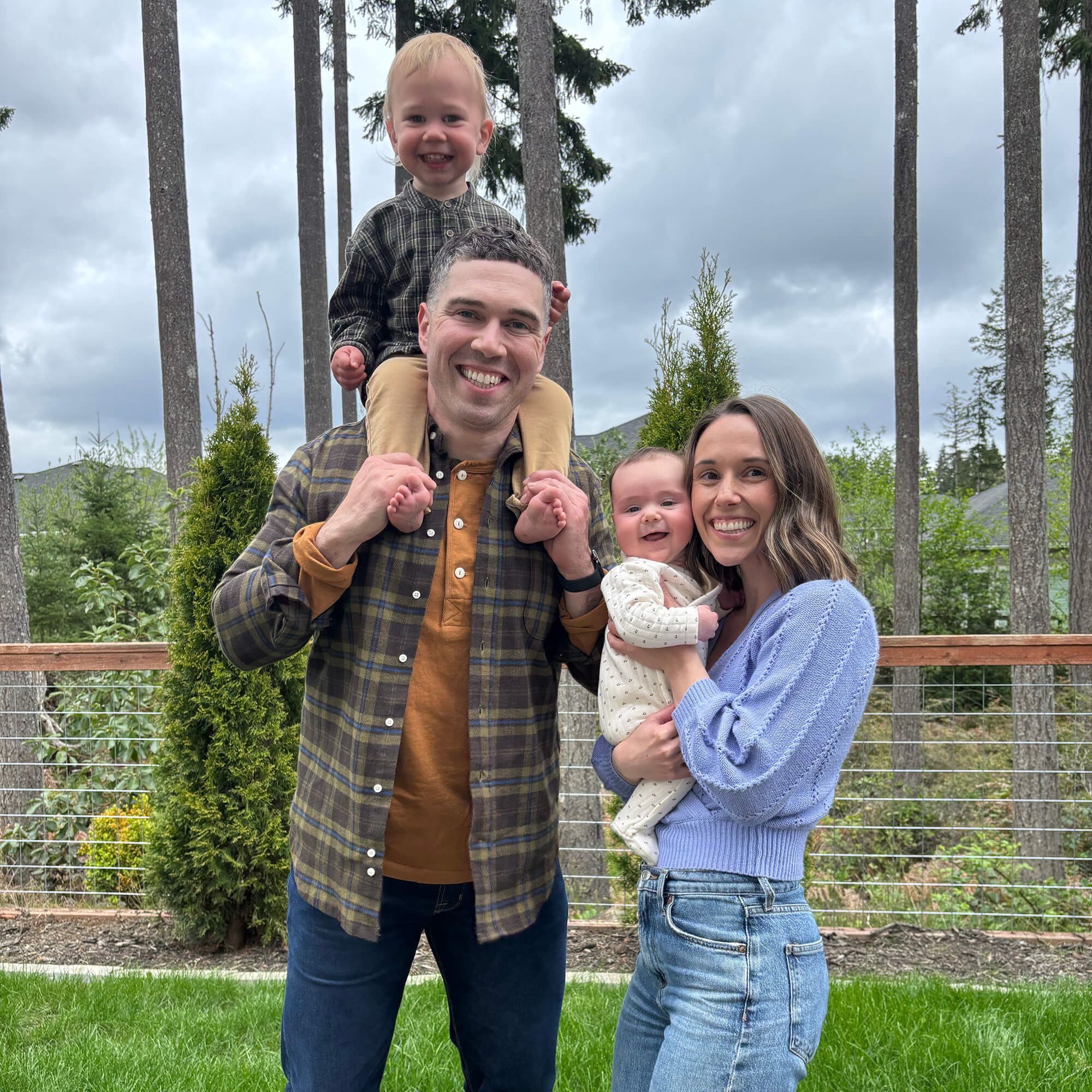 Family with two young children outdoors—dad carrying toddler on his shoulders and mom holding baby—showing the joy and challenges of parenting two under two.