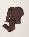 A two-piece baby pajama set in dark brown, featuring a long-sleeve top and matching footed pants, laid flat on a light beige background.