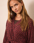 A woman wearing a dark pink patterned wrap robe with a tie waist, photographed against a plain beige studio background.