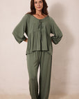 A woman modeling a matching two-piece lounge set in olive green, featuring a loose long-sleeve top with a tie neckline and matching wide-leg pants, set against a plain beige studio background.