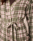 A close-up of a plaid wrap-style top or robe with a tie waist, featuring green, white, and burgundy lines over a dark brown undershirt.