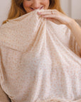 Woman holding light beige fabric with small pink floral pattern, wearing an engagement ring on left hand.