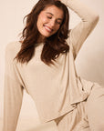 A woman wearing a cozy beige long-sleeve top and matching pants, posing in a warm neutral studio setting.