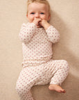 A baby lying on a beige textured blanket, wearing a cream-colored long-sleeve romper and matching pants with a small red star pattern.