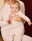 A baby and mother wearing matching long-sleeve pajamas with a small red star pattern on a cream background, posed against a dark red background.