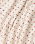 A close-up of a cream-colored fabric with a repeating pattern of small red snowflake-like motifs, shown with soft folds.