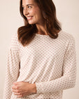 A woman wearing a cream-colored long-sleeve top with a small red star pattern, photographed against a solid light beige background.