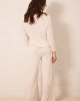 A woman shown from the back wearing a matching long-sleeve pajama top and wide-leg pants set in a light cream color with a small red star pattern, set against a plain beige studio background.