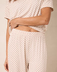A close-up of a person wearing a matching two-piece loungewear set with a short-sleeve top and wide-leg pants, both in a light cream fabric with a small red star pattern.