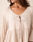 A close-up of a woman wearing a cream-colored long-sleeve blouse with a small red star pattern and a tie-front neckline.