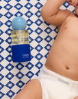 Baby lying on a blue and white checkered sheet with a bottle of Coterie product nearby.