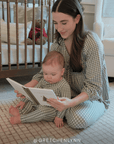 Woman and baby in matching green and white gingham sleep sets reading a book in a nursery. Features the instagram handle @gretchenlynn
