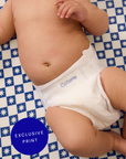 Baby wearing a white diaper on a blue and white checkered sheet with text overlay