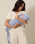 Woman holding a baby wrapped in a blue and white patterned swaddle and wearing a matching hat against a beige background