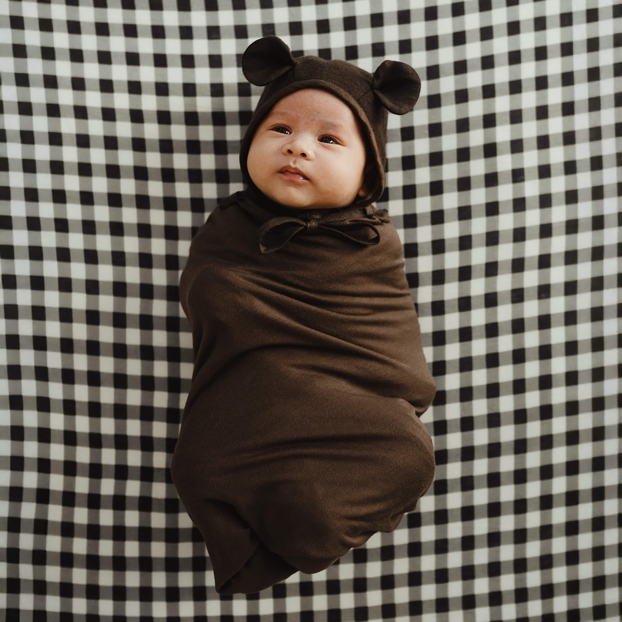 Baby is dressed like a bear cub for Halloween in the Cacao Solly Swaddle and a hat with ears