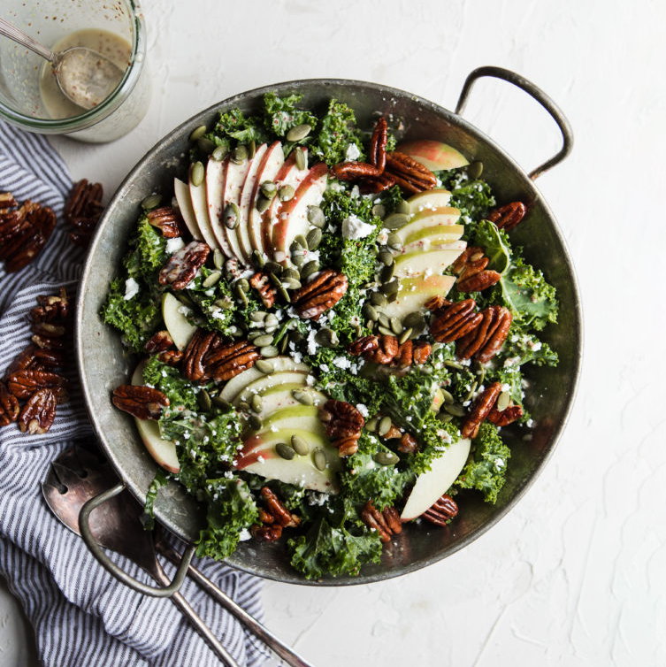 Kale salad with apples, pecans, and poppyseed dressing on a marble countertop