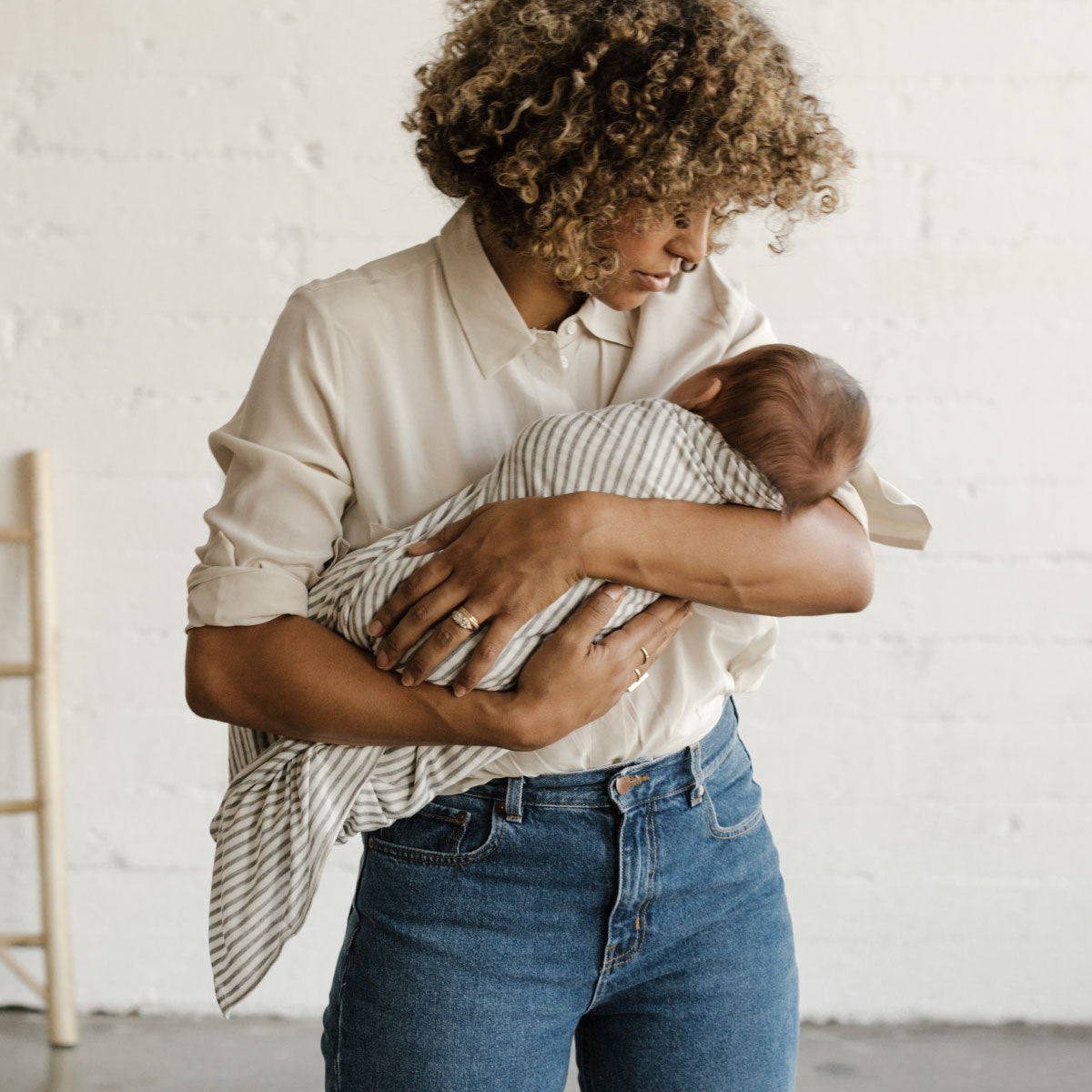 Woman looks lovingly down at baby swaddled in the driftwood stripe Solly swaddle in her arms