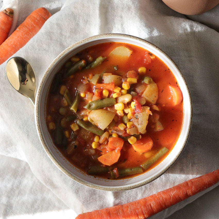 Bowl of vegetable soup on a linen napkin with a golden spoon and raw carrots placed around the bowl