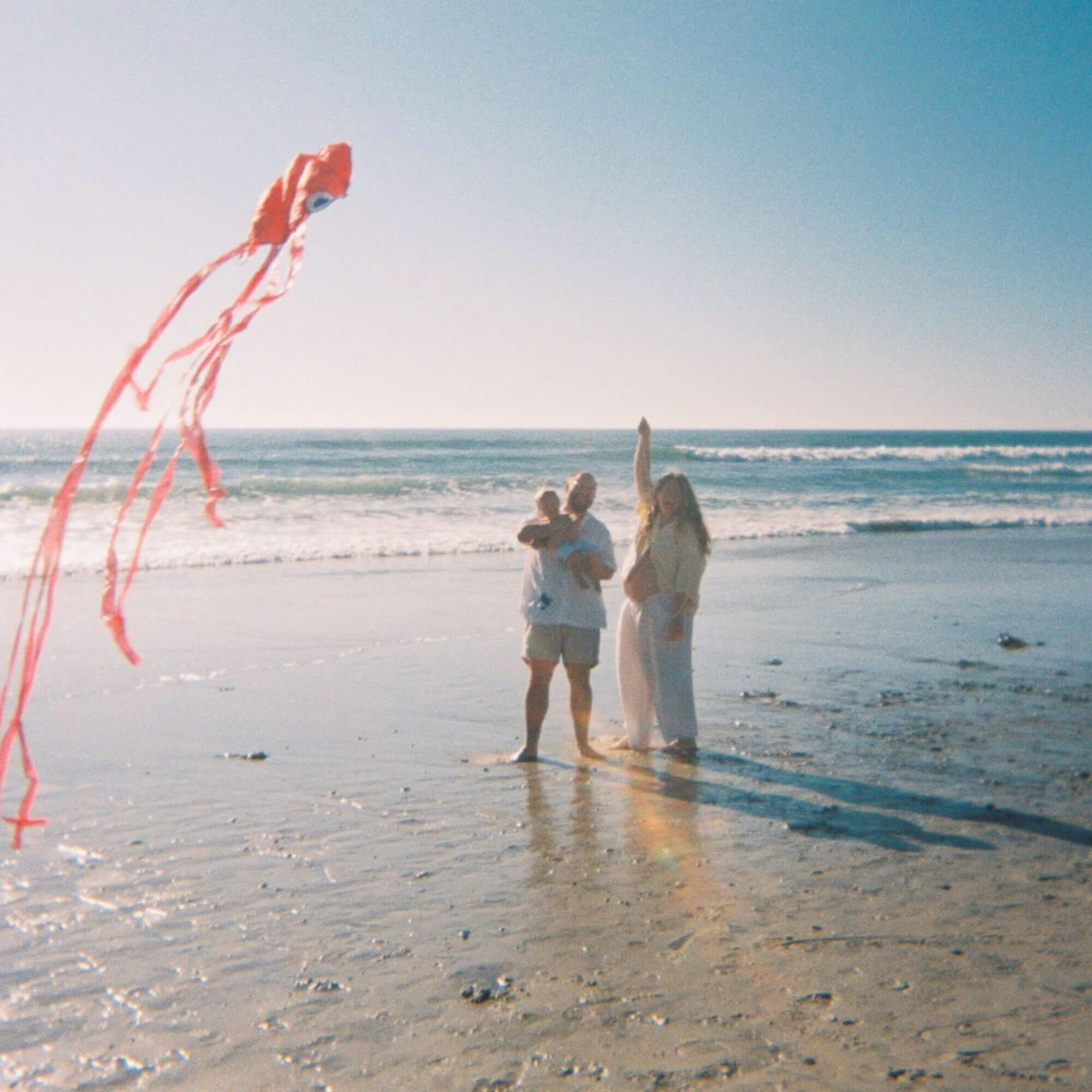 Pregnant woman and family flying kite on beach during a joyful moment.