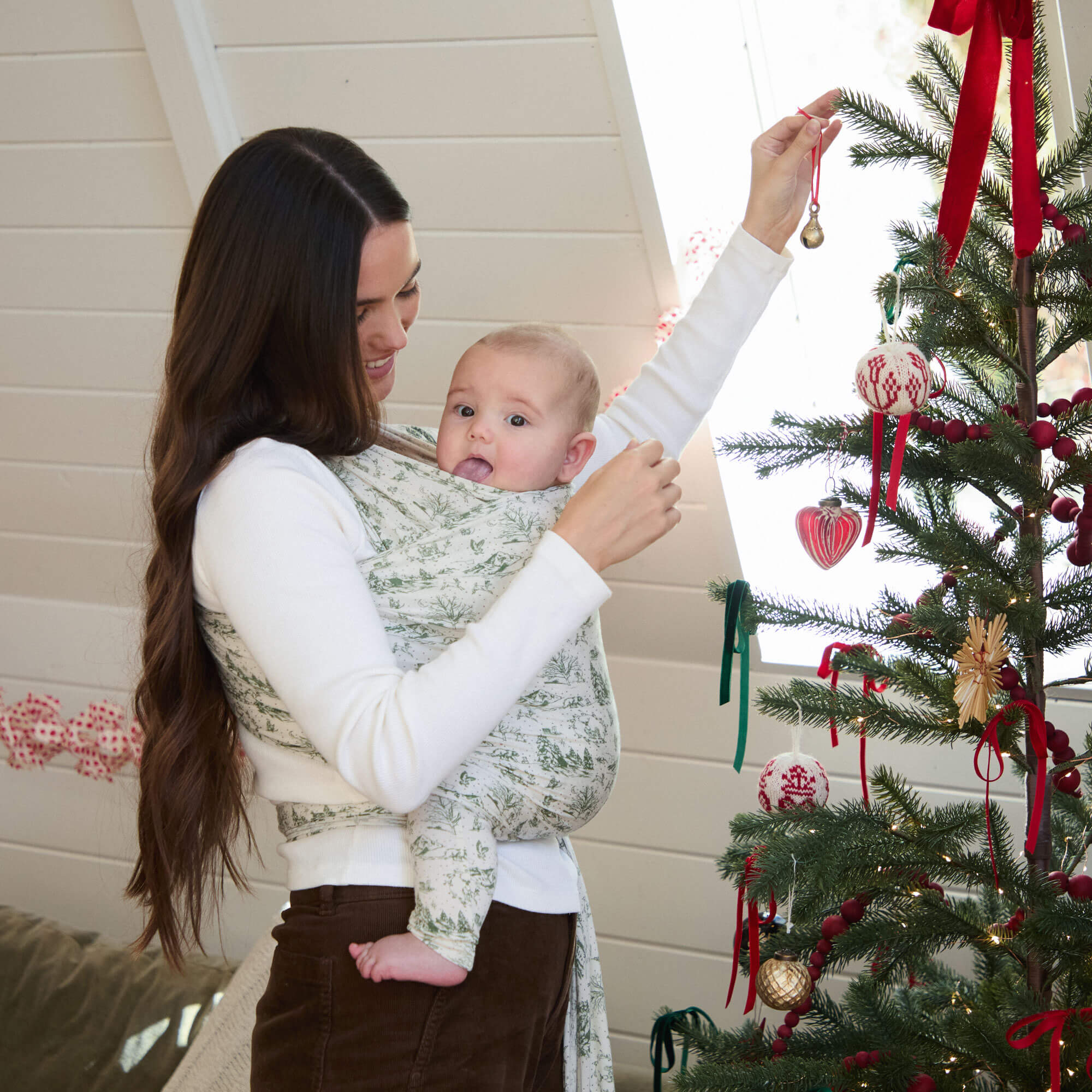 Mother watches as father holds baby up to the top of a Christmas to help decorate