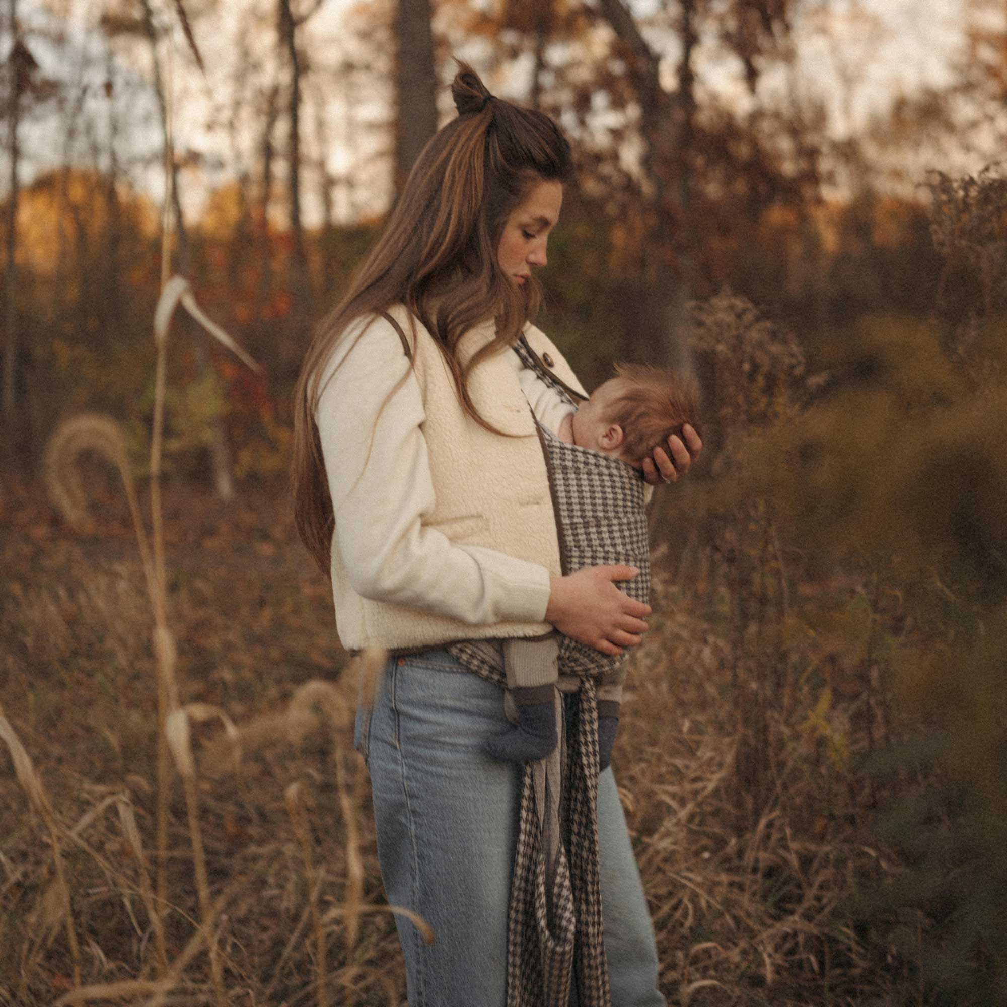 Woman nurses her baby outdoors in a field in the Stormy Houndstooth Solly Wrap