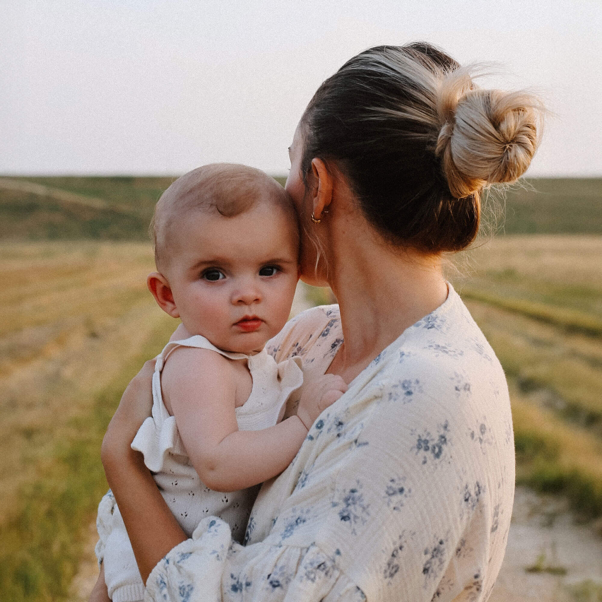 Mother holding baby on country road at sunset.