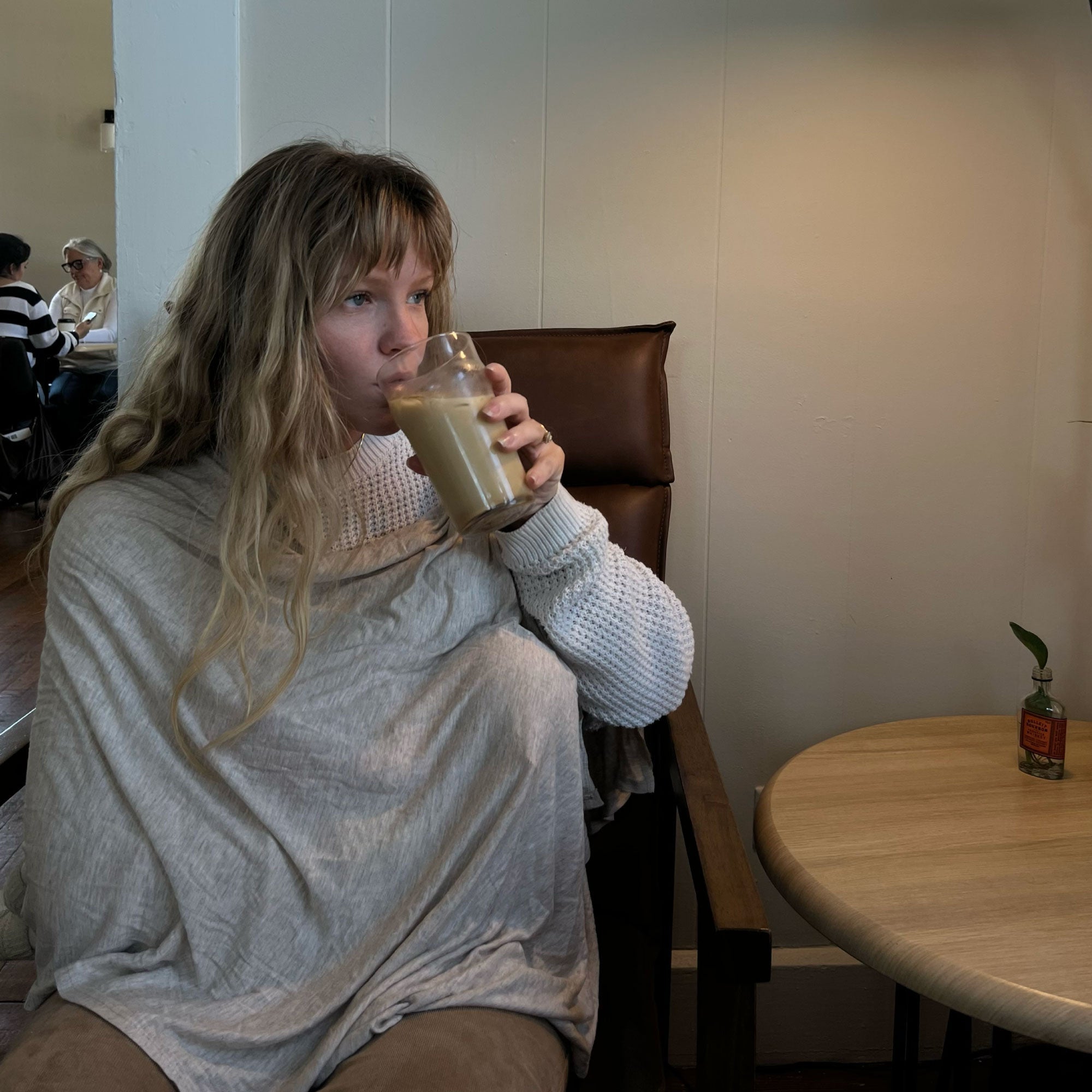Mom nursing with Solly Nursing Cover in Flax while drinking coffee at a café.