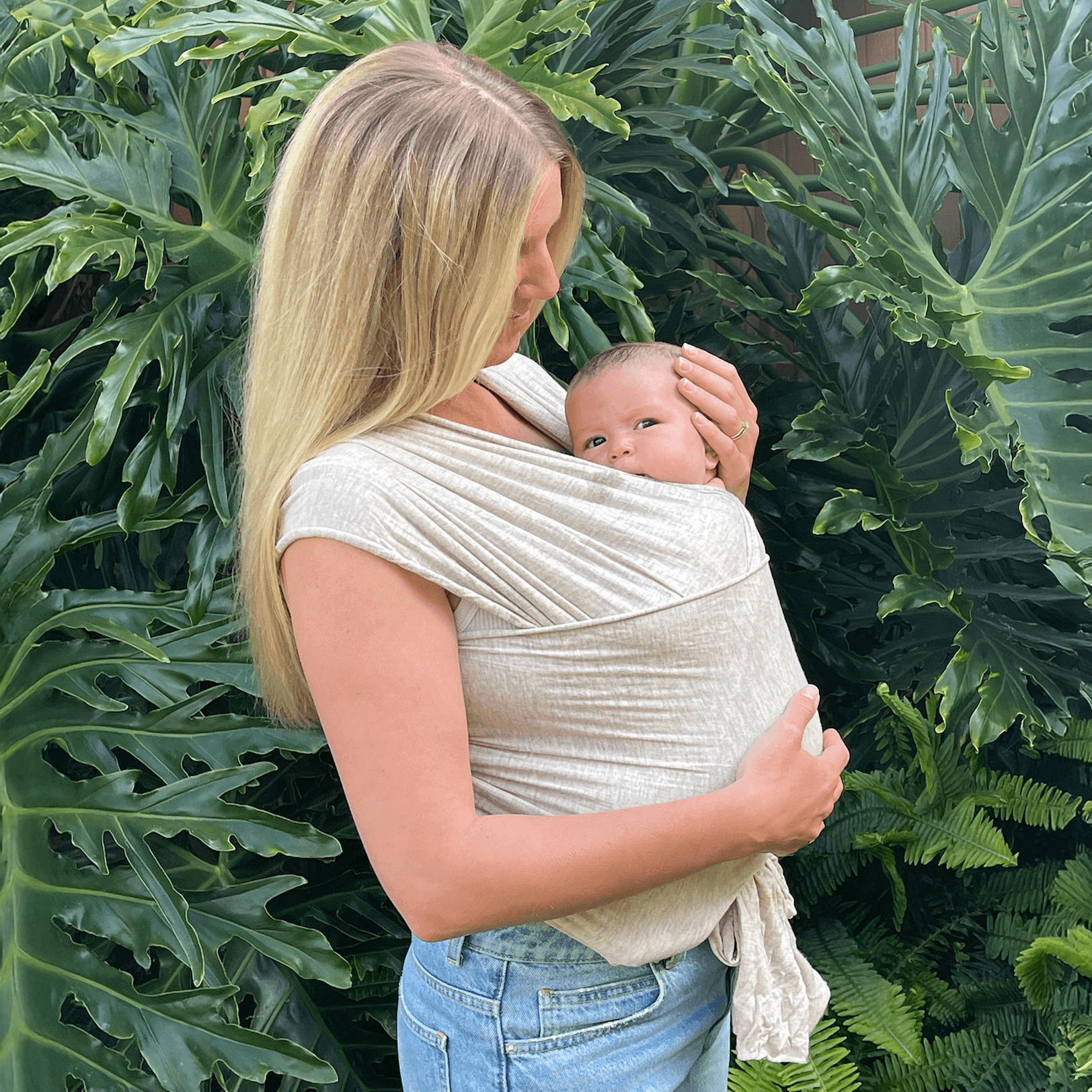 Mother cradling her infant in the Flax Solly Baby Wrap against lush greenery, demonstrating closeness and soothing benefits of babywearing.