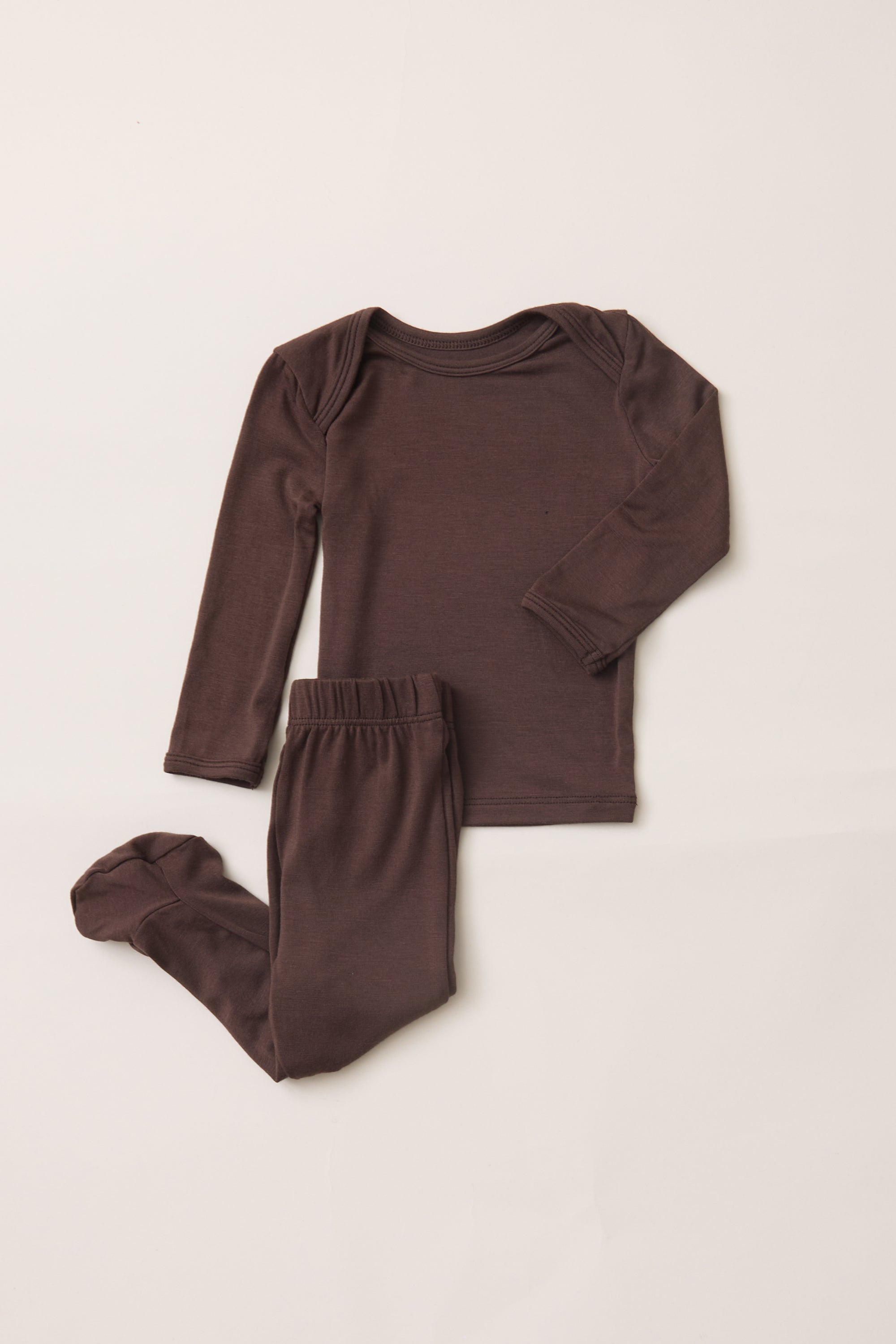 A two-piece baby pajama set in dark brown, featuring a long-sleeve top and matching footed pants, laid flat on a light beige background.
