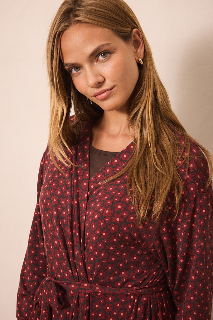 A woman wearing a dark pink patterned wrap robe with a tie waist, photographed against a plain beige studio background.