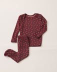 A two-piece baby pajama set featuring a long-sleeve top and footed pants in a dark red or burgundy fabric with a small pink floral pattern, laid flat on a light beige background.