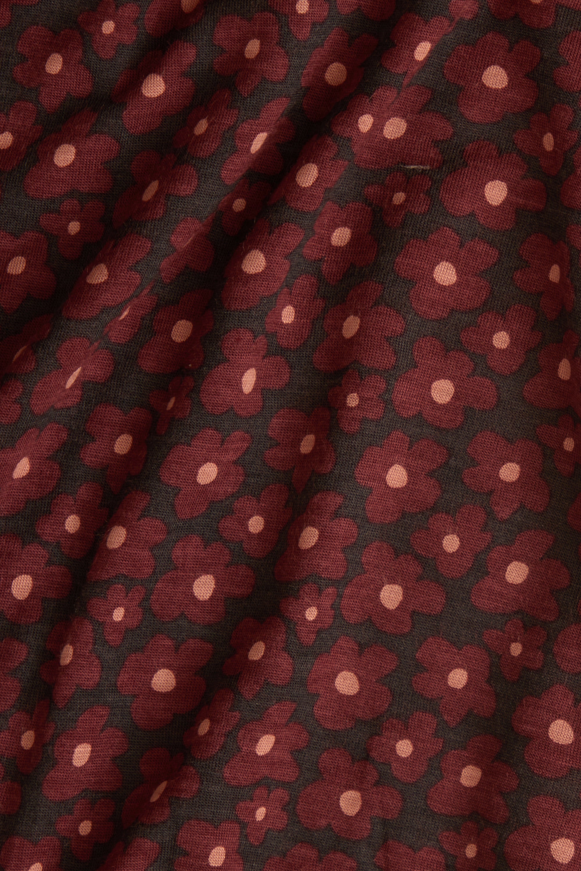 A close-up of a draped fabric with an allover floral pattern. The design features dark red flowers with light pink centers on a black background.