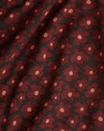 A close-up of a draped fabric with an allover floral pattern. The design features dark red flowers with light pink centers on a black background.