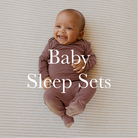 A happy baby lies on a soft, neutral backdrop, dressed in a snug, long-sleeved Solly Baby sleeper in a warm, earthy tone. Shop Baby Sleep Sets.