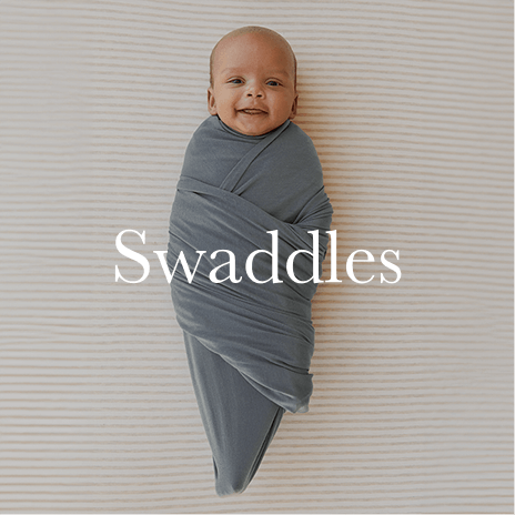 A smiling baby is securely wrapped in a Solly Baby swaddle in a deep blue shade, snug and soothed for restful sleep. Shop swaddles.