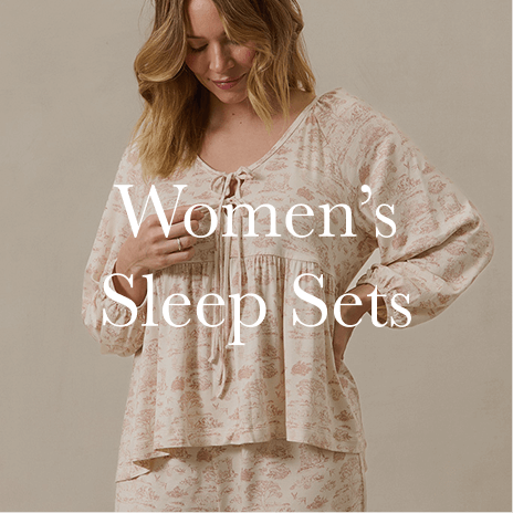 A mother wears a delicate, floral-patterned women’s sleep set, buttoning up her top for a perfect blend of function and comfort. Shop Women's Sleep Sets.