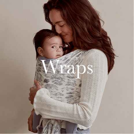  A mother cradles her baby close in a soft, patterned Solly Baby wrap, creating a cozy, hands-free moment of connection. Shop Wraps.