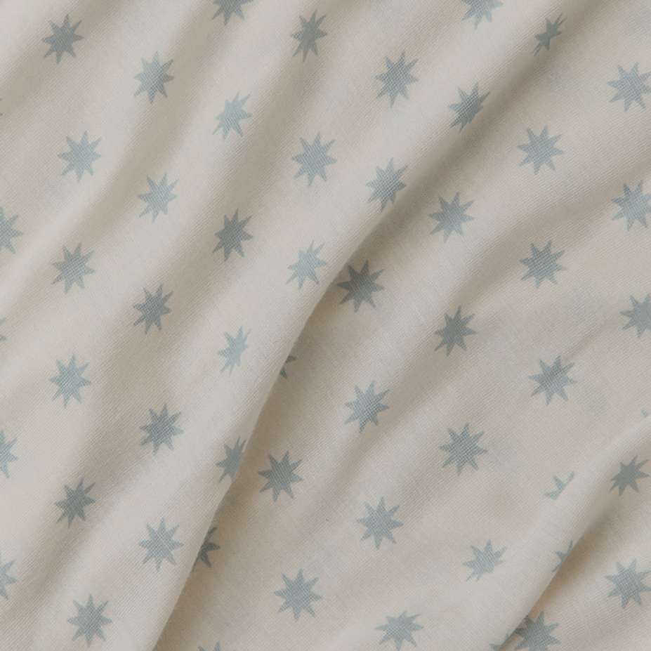 Close-up of Solly Baby's signature fabric in the Starburst colorway, showcasing delicate blue starbursts scattered across a creamy white backdrop. The fabric’s soft texture and subtle pattern create a whimsical, modern look ideal for wraps, swaddles, or cozy garments.