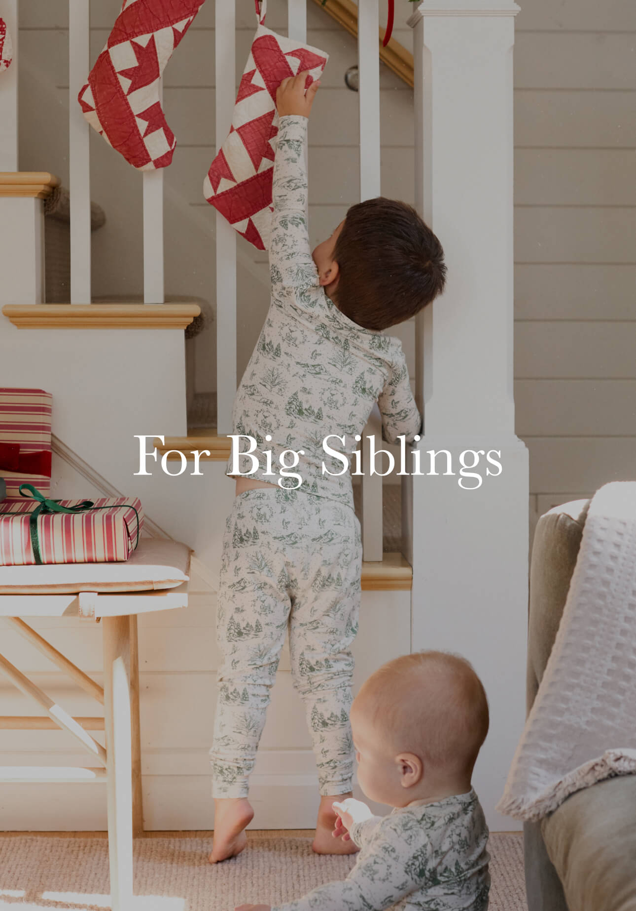 Young child in pajamas reaching for a Christmas stocking on the staircase, with a baby nearby.