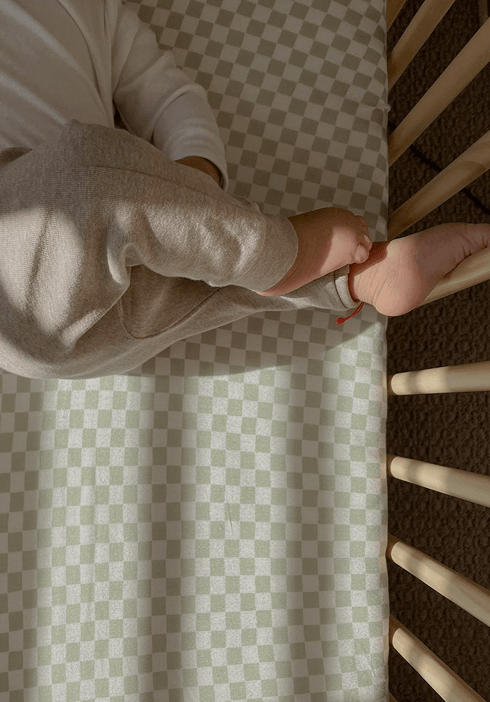 Baby resting on a Solly Baby crib sheet with a calming sage green checkerboard pattern. Soft, breathable fabric designed to provide a cozy and restful sleep.