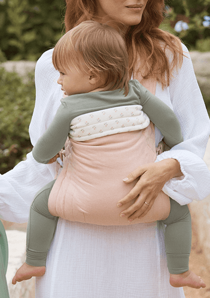 Woman holding a child in a pink buckle baby carrier with a blurred outdoor background