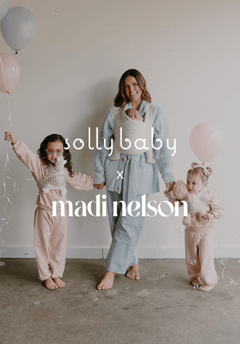  Mother smiling with her two daughters, dressed in soft pastel pajamas, while baby rests in a Solly Baby wrap worn by the mother. A joyful family moment showcasing the Madi Nelson collaboration with thoughtful designs for comfort and connection.