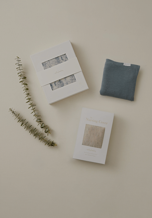 Flat lay of Solly Baby essentials, featuring a Toile wrap, a cozy charcoal swaddle, and a neutral-toned nursing cover. Thoughtful gifting and everyday comfort made simple.