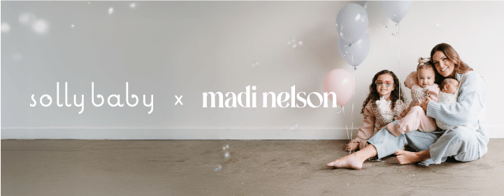 Solly Baby x Madi Nelson collaboration featuring Madi Nelson sitting on the floor with her two daughters, surrounded by soft balloons and a dreamy, neutral-toned backdrop. A celebration of motherhood, comfort, and connection.