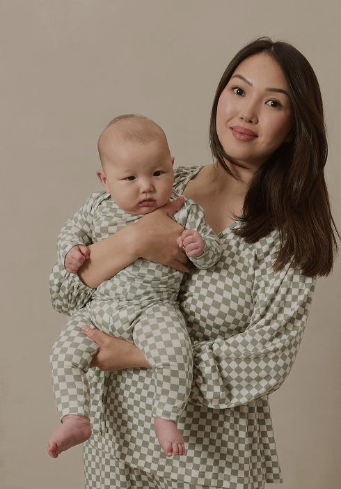 Mother holding her baby, both dressed in matching Solly Baby pajamas featuring a soft sage green checkerboard pattern. Cozy, breathable loungewear designed for sweet snuggles and restful nights.