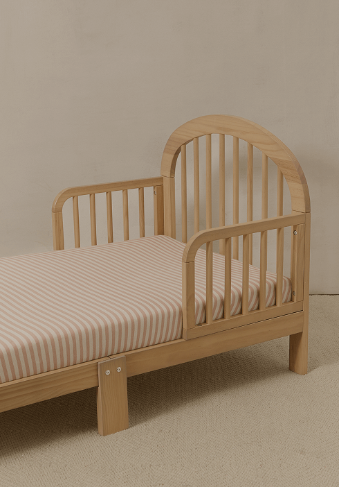 Wooden toddler bed with a Solly Baby fitted sheet in soft blush and cream stripes. Gentle, breathable fabric designed for cozy naps and peaceful sleep.