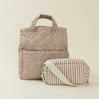 A perfectly quilted Totepack in a warm taupe floral print stands tall against a neutral backdrop. A smaller matching crossbody bag sits alongside, showcasing a coordinating taupe and cream stripe pattern with an ivory strap—designed to carry all the essentials with beauty and ease.