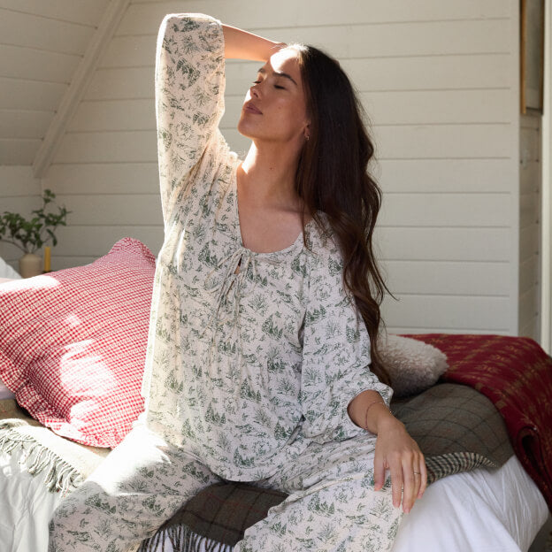 Woman stretching on bed in a soft, winter toile-printed lounge set, enjoying a calm morning light.