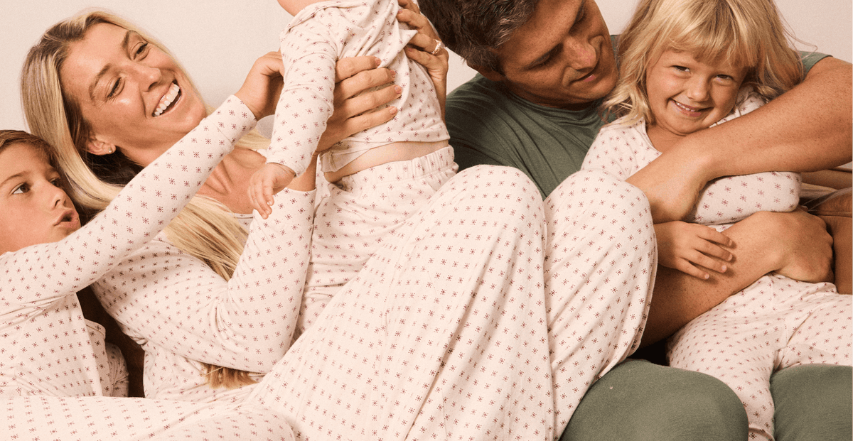 A family of four wearing matching light red pajamas with a small star pattern, lounging together on a couch in a warm, cozy setting.